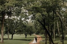 a bride and groom standing on a dirt road surrounded by trees in the middle of a lush green field