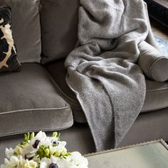 a couch with a blanket on top of it next to a coffee table and flowers