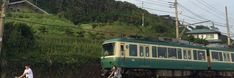 a green train traveling down tracks next to a lush green hillside