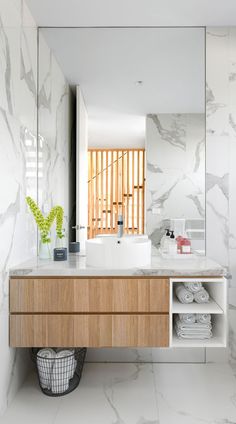 a bathroom with white marble walls and wooden cabinetry, along with a large mirror on the wall