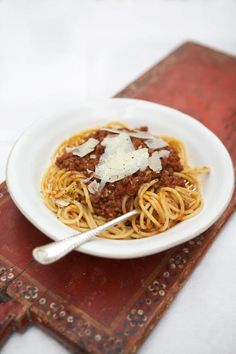 a white bowl filled with spaghetti and sauce on top of a wooden table next to an old book