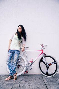 a woman leaning against a white wall next to a red and black bike with wheels