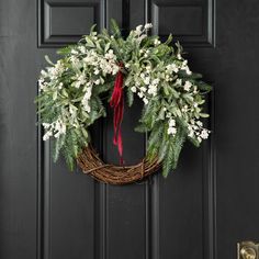 a wreath with white flowers and greenery hangs on the front door to welcome guests