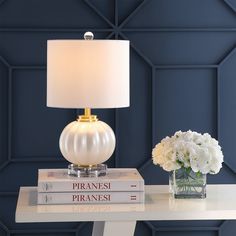 a white table with two books and a lamp on it next to a vase filled with flowers