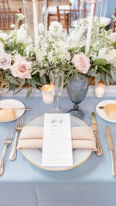 the table is set with silverware and white flowers in vases, candles, and menu cards