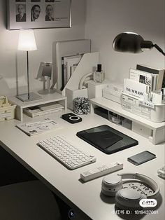 a white desk topped with a computer monitor and keyboard next to a lamp on top of a table