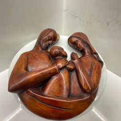 a wooden carving of two people holding a child on top of a white tablecloth