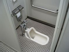 a bathroom stall with a urinal and toilet paper dispenser on the floor