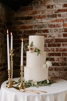 a white wedding cake with flowers and candles on a table in front of a brick wall