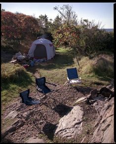 there are two chairs and a tent on the side of a hill with trees in the background