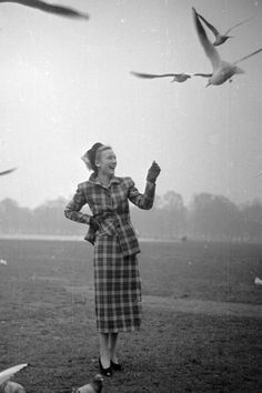 a woman standing on top of a grass covered field next to birds flying over her