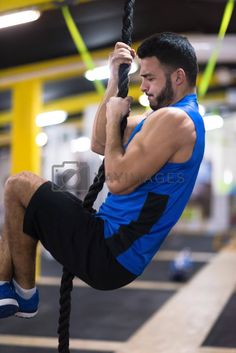 a man hanging from a rope in a gym with his feet up on the ground