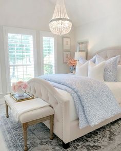 a white bed sitting in a bedroom next to a window with a chandelier