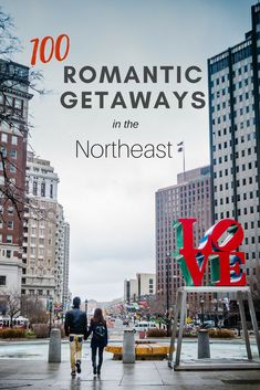 two people walking down the street in front of some tall buildings and a love sculpture