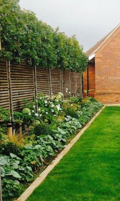 a garden with green grass and flowers next to a brick building on a cloudy day