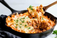 a wooden spoon scooping some food out of a skillet filled with lasagna