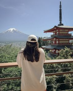 a woman standing on top of a balcony next to a tall building with a mountain in the background