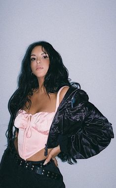 a woman with long black hair wearing a pink top and black pants, posing for the camera