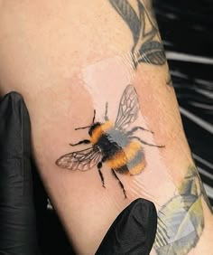 a bee tattoo on the left arm and right hand with black gloves holding it up