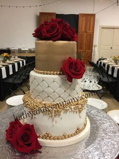 a three tiered wedding cake with red roses on the top and gold trimmings