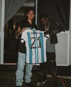 two men holding up a soccer jersey in front of a window