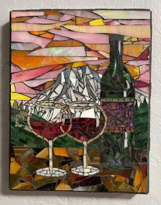 a stained glass panel with two wine glasses and a mountain in the background, on a white wall