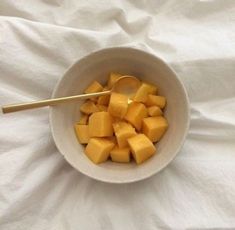 a white bowl filled with cut up pieces of cheese and a wooden spoon in it