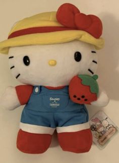 a hello kitty stuffed animal with overalls and a strawberry on it's chest