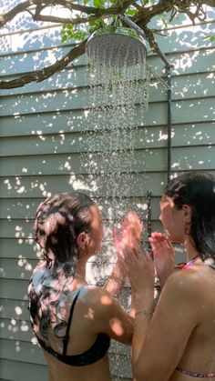 two women in bathing suits standing under a shower head and spraying water on their faces