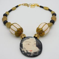 This 1 of a kind necklace features alovely handmade ceramic Geisha pendant made by an American artist.  Pendant is about 2 inches in height x 1 3/4 inch in width. Back of pendant is finished with black and cream splotched/swirled pattern.  Pendant hangs from necklace made with fancy brass beadcaps, large handmade vintage brass and resin focal beads from Nepal, very nice handmade brass beads fro Nigeria,  These beads were shaped entirely by hand using hammer...I love the way they show hammer marks.  I have also used 4 Mongolian Jet beads and tiny black glass beads. Necklace fastens with my signature large fancy brass clasp and very nice textured goldplated chain. Length adjusts from about 19 - 21 inches. Unique White Jewelry For Art Collection, Artistic White Necklace With Unique Variations, Artistic White Round Necklace, White Hand Painted Round Necklace, White Hand Painted Round Necklaces, Bohemian White Hand Painted Necklace, Hand Painted Artisan Jewelry With Round Beads, Artistic Round Beads Necklace For Gift, Artisan Hand Painted Round Bead Jewelry