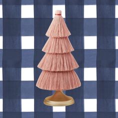 a small pink christmas tree sitting on top of a wooden stand in front of a blue and white checkered wall