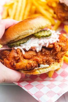 a hand holding a chicken sandwich with pickles and mayonnaise on the side