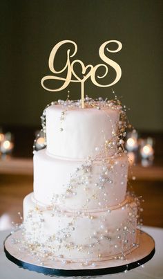 a three tiered cake with the initials on top is decorated with pearls and sparkles