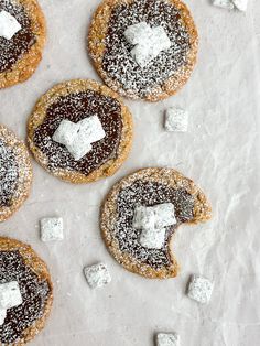 four cookies with marshmallows on them and some sugar cubes scattered around