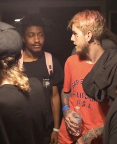 a group of young men standing around each other in a dark room with one man holding a drink