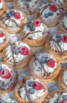 a tray filled with lots of desserts covered in frosting and berries on top