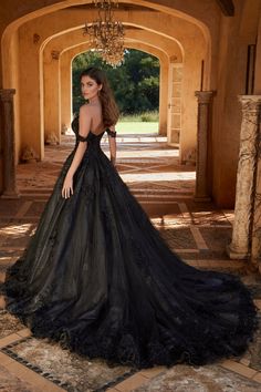 a woman in a black dress standing on a stone floor with an archway and chandelier