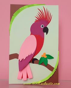 a pink and green bird sitting on top of a tree branch next to a piece of paper