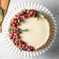 a cheesecake with cranberries and rosemary sprigs on top sits on a white plate