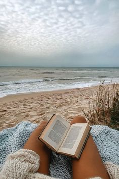 an open book sitting on top of a person's lap next to the ocean