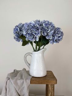 a white vase filled with blue flowers sitting on top of a wooden table next to a blanket