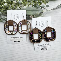 three wooden earrings with different designs on them sitting next to each other and some flowers