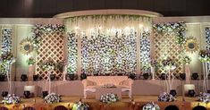 a stage set up for a wedding with flowers on the wall and chandelier