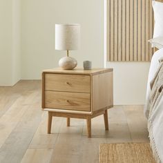 a nightstand with two drawers and a lamp on it in a bedroom next to a bed