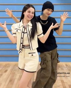 two people standing next to each other in front of a blue wall with their hands up