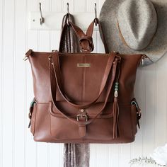 two brown purses are hanging on the wall next to a hat and flower vase