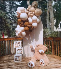 a brown teddy bear sitting on top of a wooden deck next to a bunch of balloons