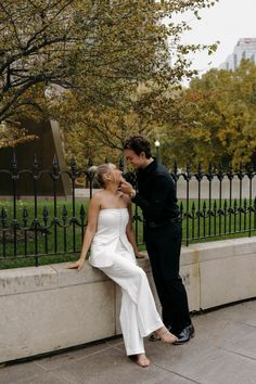 a bride and groom standing next to each other in front of a wrought iron fence