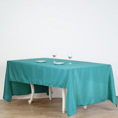 a table with two wine glasses on it in front of a white wall and wooden floor