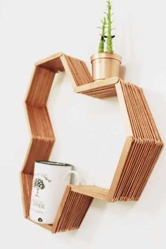 a wooden shelf holding a potted plant next to a cup on a white wall